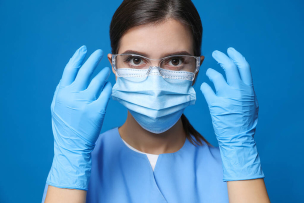 Doctor in protective mask, medical gloves and glasses against blue background - Photo, image