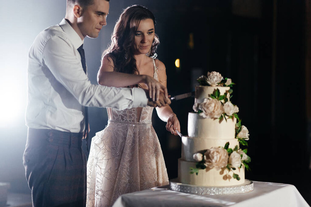 Koncentrált friss házasok, akik háromszintes esküvői tortát vágnak virágokkal díszítve. Esküvői parti. Boldog menyasszony és vőlegény. Kiváló minőségű fénykép - Fotó, kép