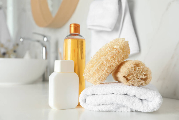 Natural loofah sponges, towel and cosmetic products on table in bathroom - Foto, Imagen