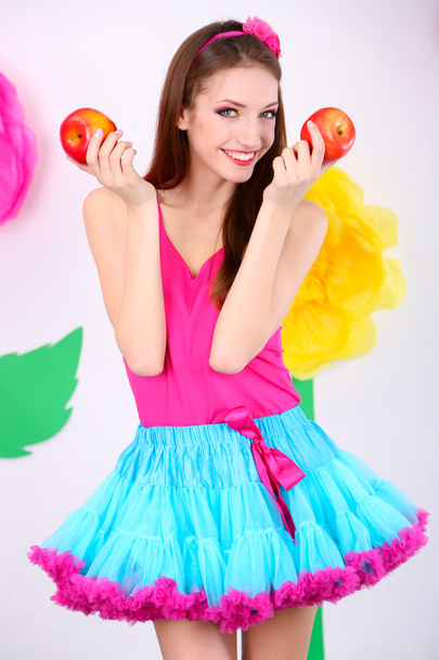 Beautiful young woman in petty skirt with apples on decorative background - Фото, зображення