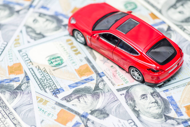 Red toy car is standing on dollar banknotes. Cost of buying a car, fuel, insurance and other car costs. - Photo, image