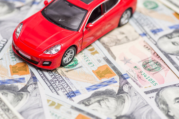 De rode speelgoedauto staat op dollarbiljetten. Kosten van het kopen van een auto, brandstof, verzekering en andere auto kosten. - Foto, afbeelding