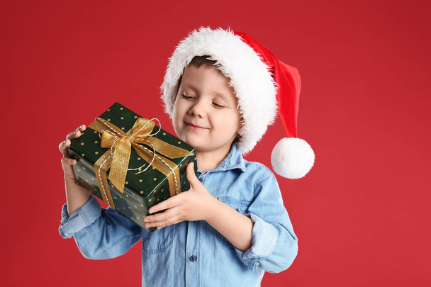 Cute child in Santa hat with Christmas gift on red background - Foto, immagini
