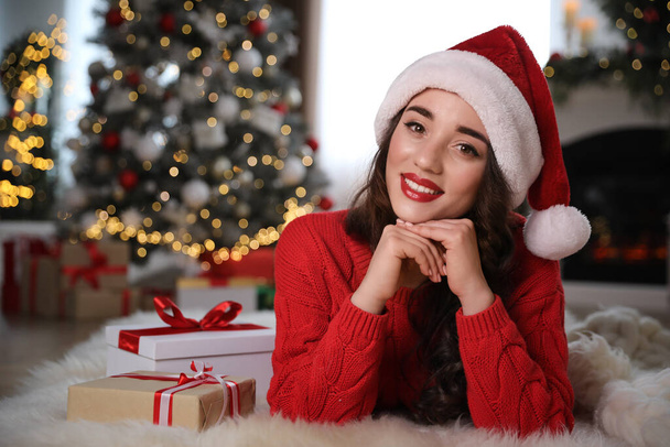 Beautiful woman wearing Santa hat with Christmas gifts on floor at home - Fotoğraf, Görsel