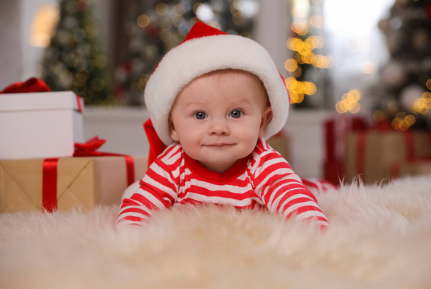 Cute little baby in bright pajamas and Santa hat on floor at home. Christmas suit - Фото, изображение