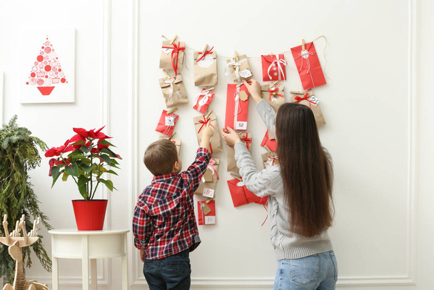 Mother and son taking gift from Advent calendar at home, back view. Christmas tradition - 写真・画像