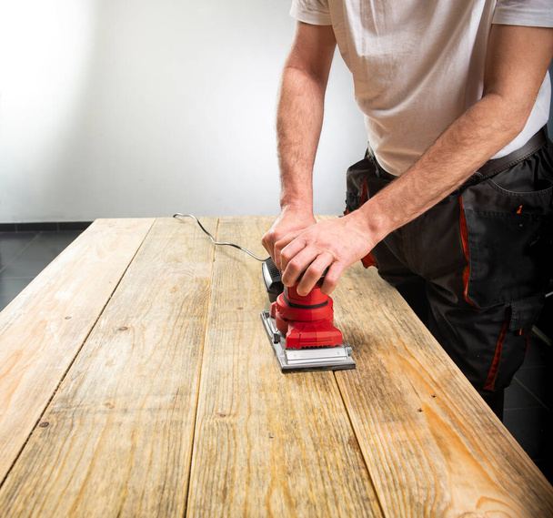 Máquina de lixar na mão masculina. Processamento de peça de trabalho em mesa de madeira marrom claro  - Foto, Imagem