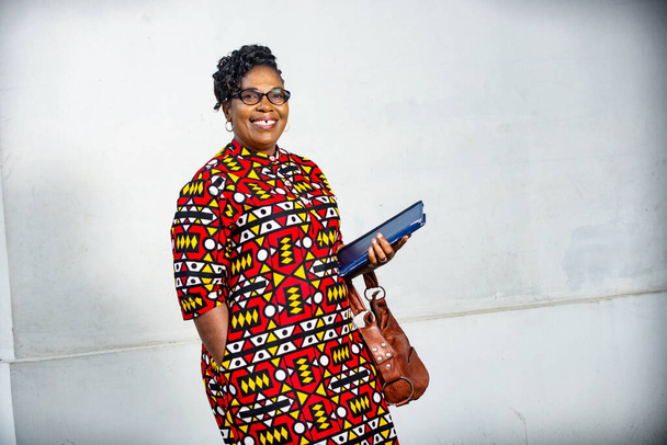 όμορφη ενήλικη επιχειρηματίας φορώντας γυαλιά και κρατώντας ένα ψηφιακό tablet και τσάντα και κοιτάζοντας κάμερα χαμογελώντας - Φωτογραφία, εικόνα