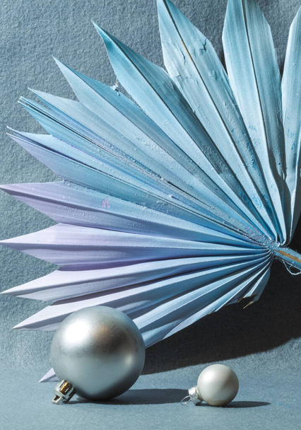 Composition abstraite avec des boules grises décoratives et une feuille de palmier peinte en bleu. Fond gris, orientation verticale, ombres dures - Photo, image