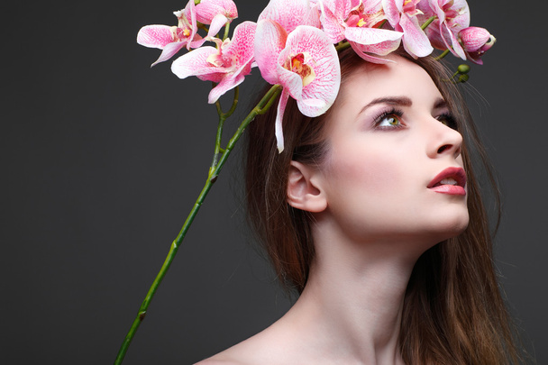 Hermosa chica, aislada sobre un fondo gris claro con orquídeas rosadas en pelos, emociones, cosméticos
 - Foto, Imagen