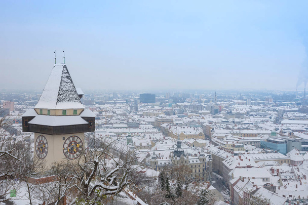 La famosa torre del reloj en la colina de Schlossberg y los edificios históricos tejados con nieve, en Graz, región de Estiria, Austria, en el día de invierno - Foto, imagen