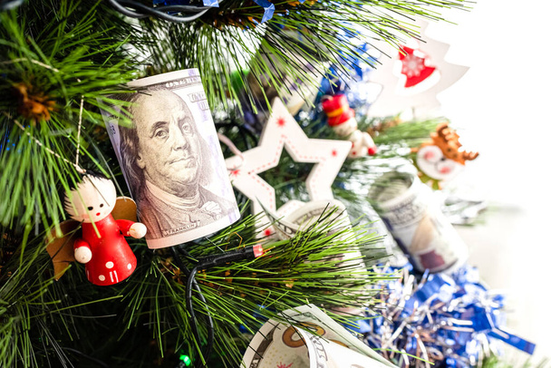 Долларовые купюры висят на елке рядом с традиционными рождественскими украшениями. - Фото, изображение