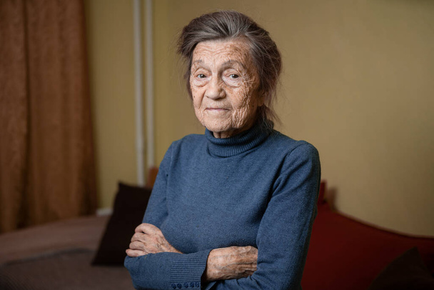 Older cute woman of ninety years old Caucasian with gray hair and wrinkled face looks at camera, cute kind look and smiles.Mature grandmother retired long-liver, theme emotion and mood of old people. - Photo, Image