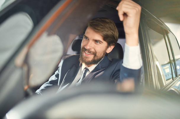Χαρούμενος άντρας με κοστούμι που οδηγεί αμάξι. Πλούσιος άντρας με συναισθήματα επιβατών. - Φωτογραφία, εικόνα
