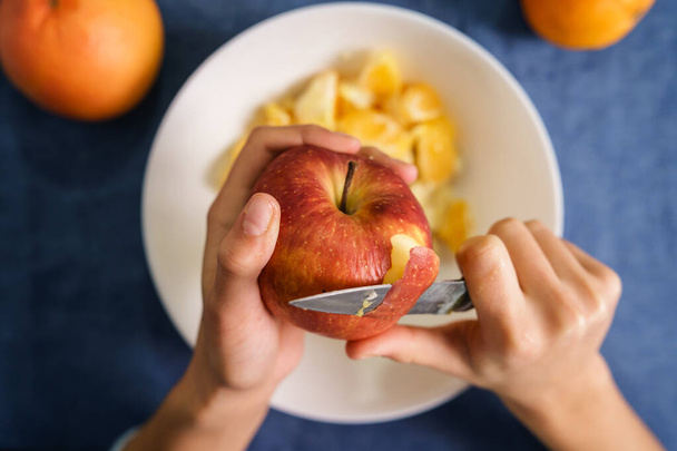 Közelkép ismeretlen kaukázusi nő kezéről, amint piros almát hámoz az asztalon lévő tál fölött otthon - egészséges táplálkozás koncepció bio étel házi vegetáriánus vagy vegán étel - felülnézet - Fotó, kép