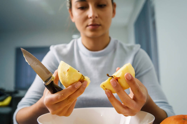 Закройте на руках кавказскую женщину, разрезающую яблоко над миской на столе дома - концепция здорового питания органические продукты домашней вегетарианской или веганской еды - Фото, изображение
