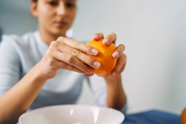 Lähikuva käsissä nuori nainen kuorinta oranssi pöydän kotona - terveellistä syömistä orgaaninen kasvisruoka käsite kopioi tilaa - Valokuva, kuva