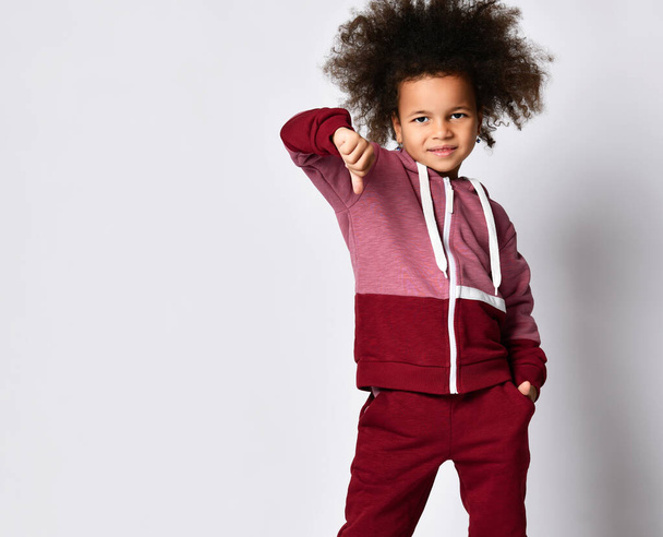 Little afro-american girl in sportswear shows thumb down standing on a gray background. - Foto, immagini