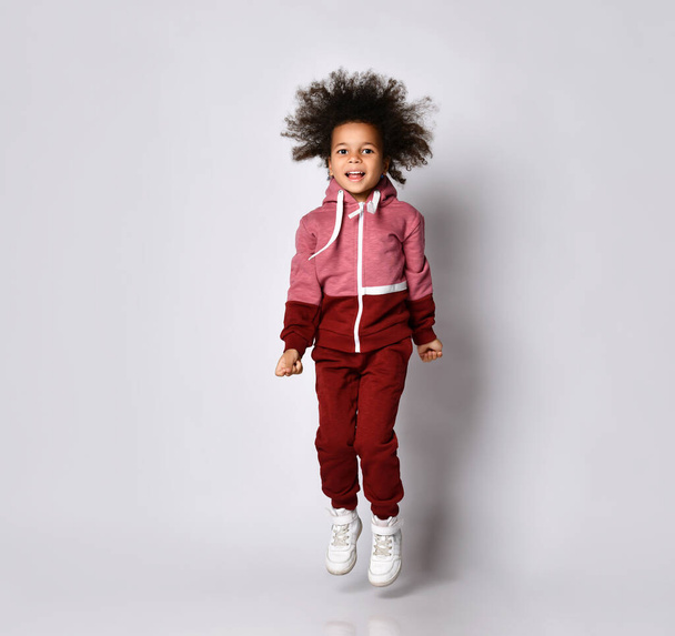 African American girl in a stylish modern red jumpsuit jumps high on a gray background. - 写真・画像