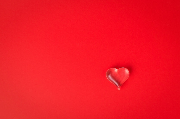 Un piccolo cuore di vetro su uno sfondo rosso brillante. Simbolo di amore e vita. - Foto, immagini