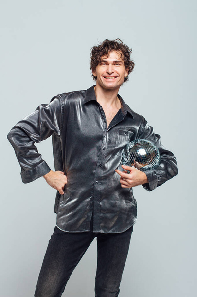Portrait of tall attractive man with a mirror disco ball on a white background. Handsome man posing with a shiny disco ball in studio. - Fotografie, Obrázek