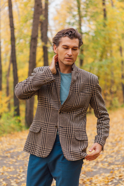 Tall handsome man dressed in a brown jacket walking on the autumn alley - Fotografie, Obrázek