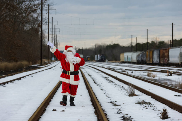 Santa Claus caminando en el camino lluvioso y agita su mano en el día de Navidad al llevar una bolsa de regalos - Foto, Imagen