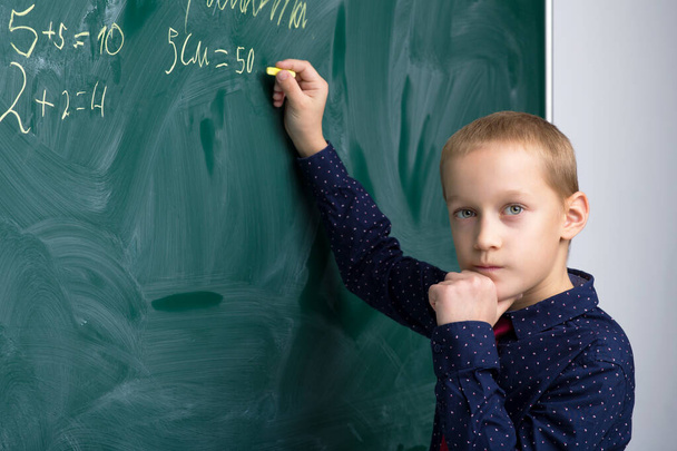 Schoolboy writing on chalkboard in classroom - Foto, imagen