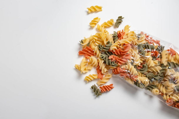 Pakiet makaronu Tricolor Fusilli otwarty makaronem wylewającym się z opakowania na białą powierzchnię. Pojęcie żywności bogatej w węglowodany. - Zdjęcie, obraz