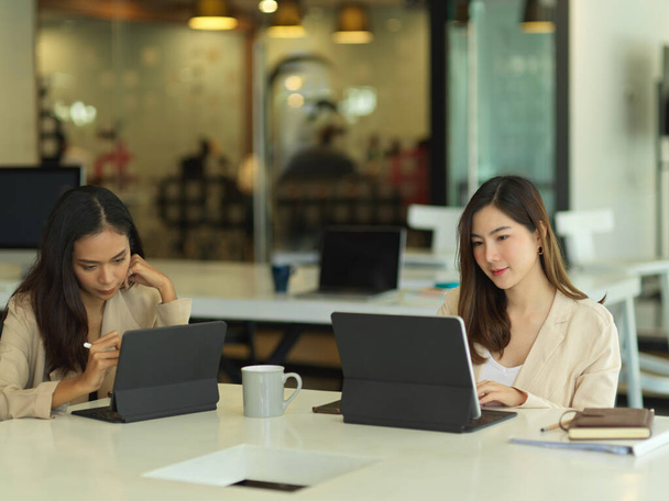 Retrato de dos trabajadoras de oficina que trabajan con tabletas digitales en la sala de reuniones - Foto, Imagen
