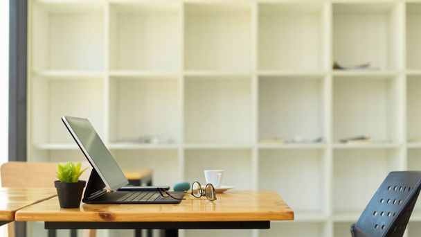 Zijaanzicht van het bureau met digitale tablet, kantoorbenodigdheden en decoratie in de kantoorruimte - Foto, afbeelding