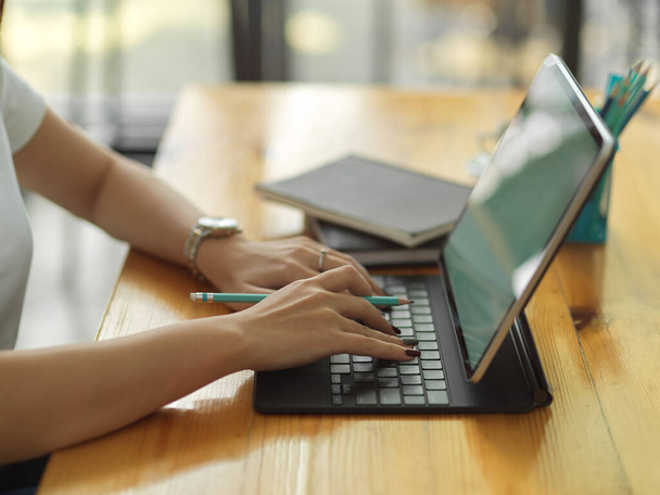 Vista laterale della digitazione femminile su tastiera tablet su tavolo in legno nella sala home office - Foto, immagini
