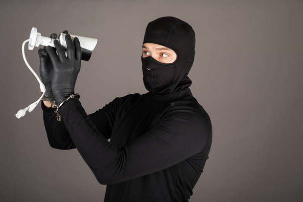 Picture of thief wearing black face mask is trying to turn off a surveillance camera - Фото, изображение