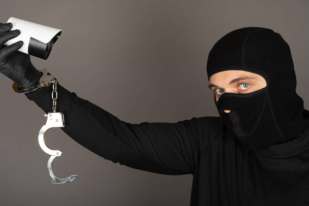 Siyah maskeli bir hırsızın fotoğrafı güvenlik kamerasını kapatmaya çalışıyor. - Fotoğraf, Görsel