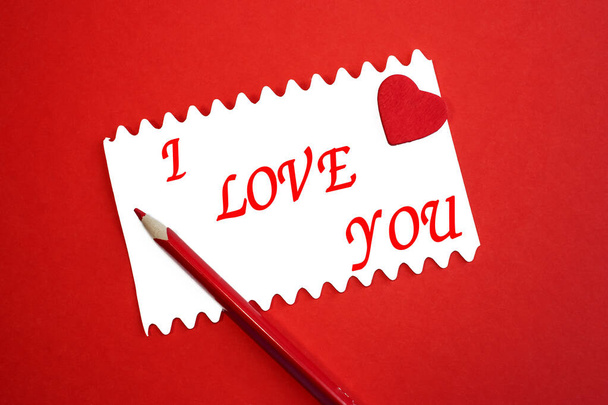 Miluji tě je napsáno na bílém listu, který leží s červenou tužkou a srdcem na červeném pozadí. Slavnostní zázemí. Valentýn - Fotografie, Obrázek