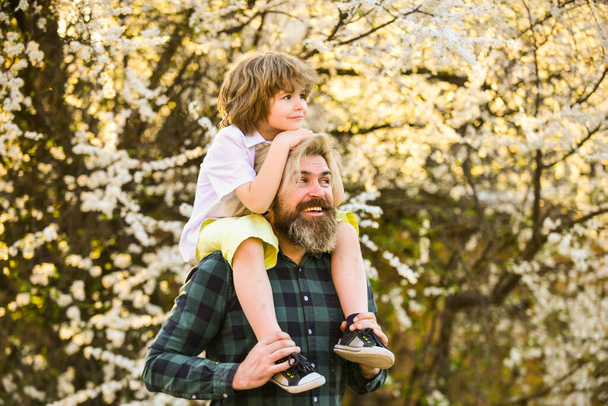 He makes him fly. father and son near sakura tree blossom. happy fathers day. celebrate childrens day together. family love and values. relax outdoor together. we are family. small kid hug his dad - Foto, imagen