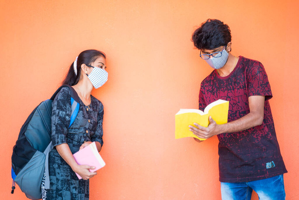 Two students in face mask discussing at college while maintaining social distance - concept of college reopen with covid-19 or coronavirus safety measures at university campus - Фото, изображение