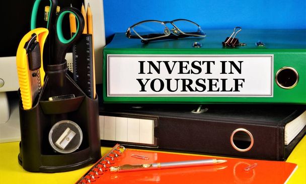 Invest in yourself. Lettering of the text in the folder on the background of stationery. Placement of capital for the purpose of obtaining financial profit or knowledge in education. - Photo, Image