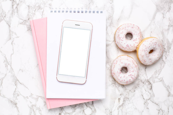 Mobile phone,pink notebook and sweet donut on a marble background flat lay, technology and sweet food top view - Valokuva, kuva