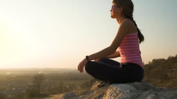 Jonge ontspannen vrouw zit buiten op een grote steen genietend van warme zomerdag. Meisje mediteren en ontspannen op de natuur bij zonsondergang. - Video