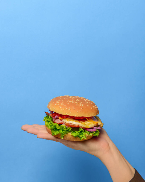 Homemade beef grilled hamburger in a hand over bright blue background. Copy space banner. Junk food, fast food concept. - Foto, Imagem