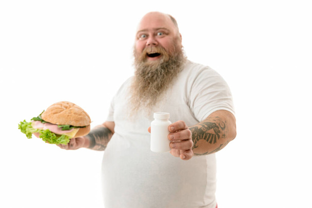 Emotional fat funny and tattooed man with food isolated on a white background - Photo, Image