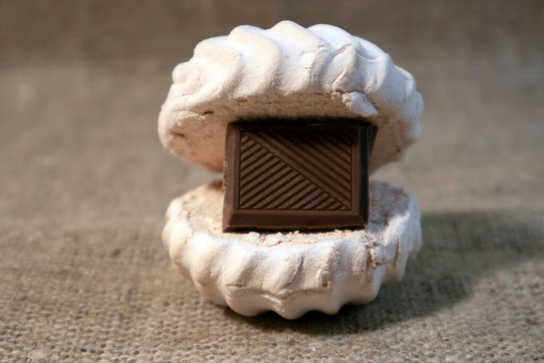 White zephyr with tile of dark chocolate inside lying on a sack cloth - Photo, Image