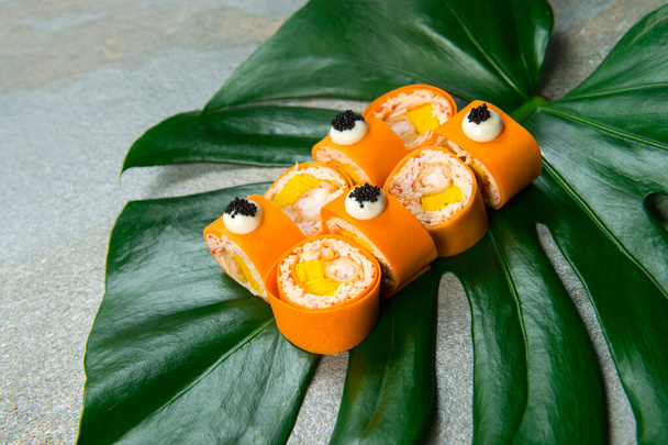 Close up to healthy Japanese no rice sushi roll with tempura black tiger shrimp (prawn) wrapped in carrot daikon served with caviar (flying fish roe) on exotic monstera leaf on gray stone background - Photo, Image