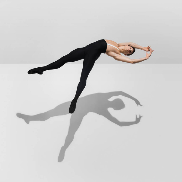 Beautiful young male athlete practicing on white studio background with shadows in jump, air flying - Φωτογραφία, εικόνα