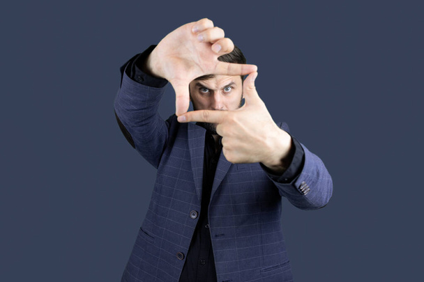 Человек в синем костюме делает рамку из пальцев и смотрит сквозь пальцы - Фото, изображение