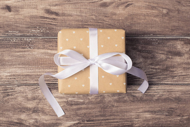 Above close up view photo of xmas christmas giftbox wrapped in craft paper with white ribbon on wood brown background - Fotografie, Obrázek