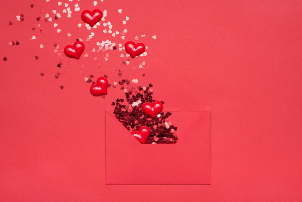 Romantische Gefühle Ausdruck Konzept. Flachbild-Foto von ausgepacktem Papierumschlag und wegfliegendem glänzenden Glitzern und Herzen auf hellem Farbhintergrund - Foto, Bild
