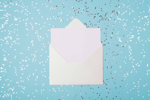 Top above flat lay close up view photo of open white envelope and sheet of paper on light pastel blue background with silver confetti - Photo, Image