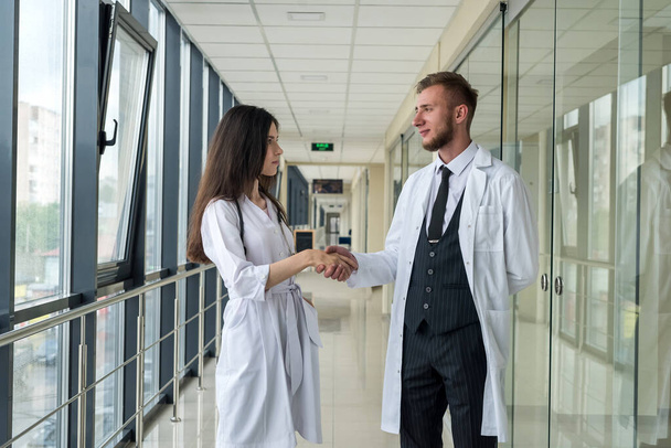 Два молодых стажера-врача позируют в коридоре современной больницы. Концепция здоровья - Фото, изображение